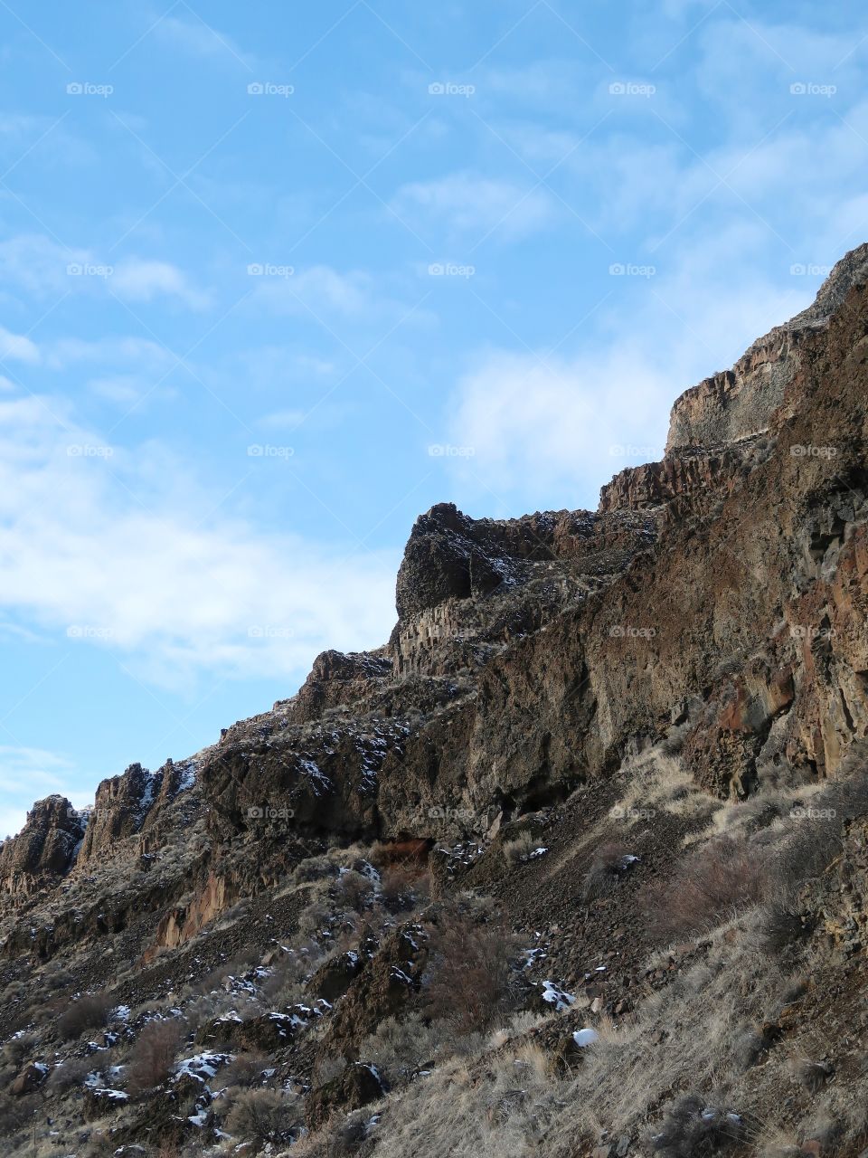 Cliffs of basalt stick out with just a bit of snow on the ground on a beautiful sunny winter day in Central Oregon. 