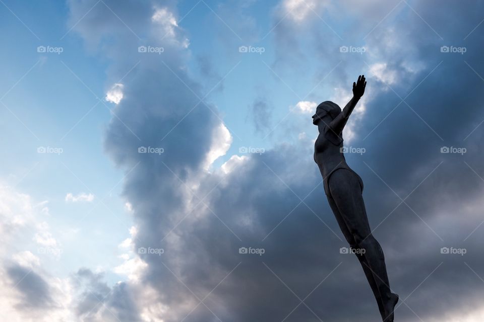 The Diver. Silhouette of a statue of a diving woman against a cloudy sky. 