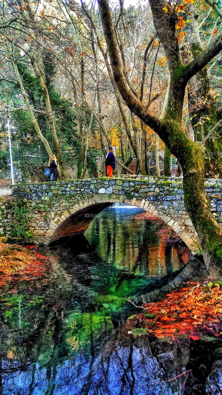 Two women are crossing a picturesque bridge in Piges Kryas in Leivadia,Greece.