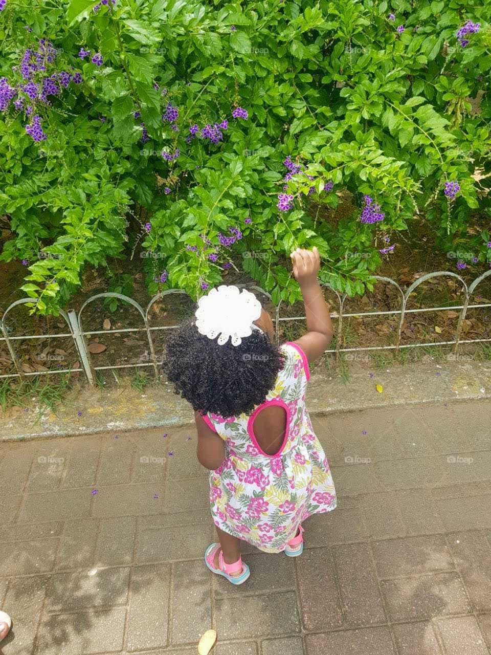 Menina brincando com flores, em um parque.