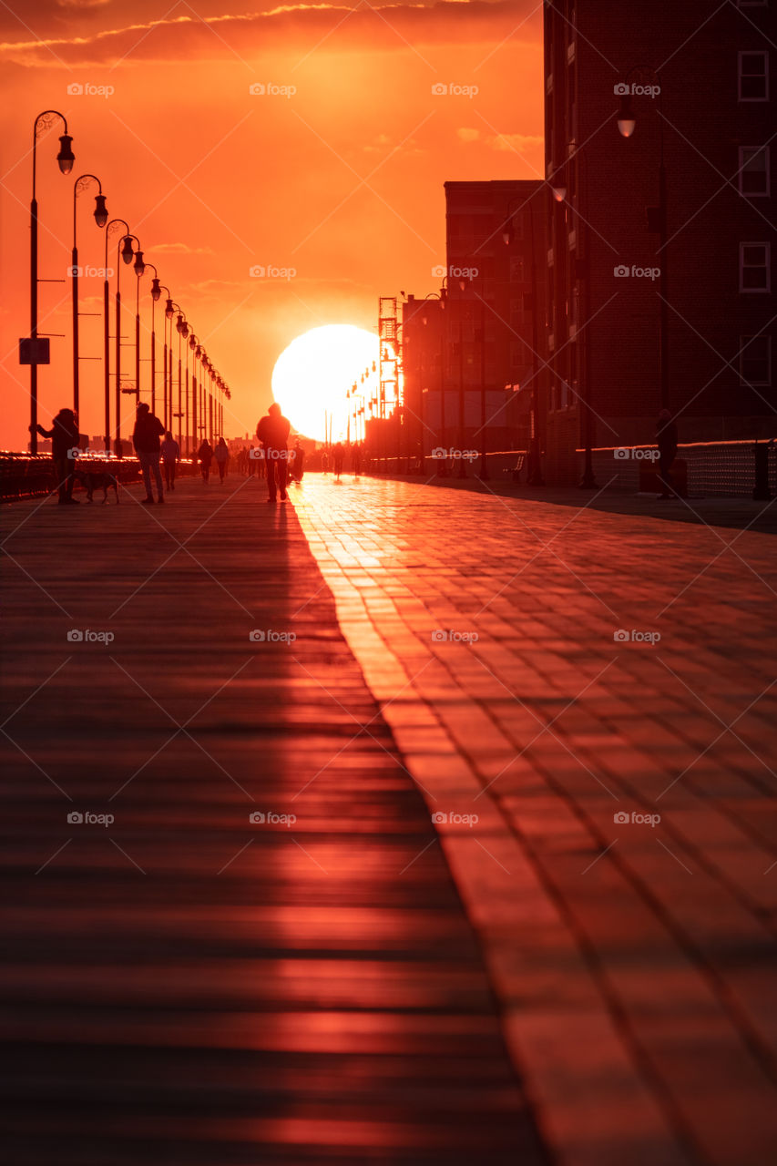 Gorgeous golden sunset at the end of a boardwalk, with lampposts and boardwalk lines leading your eye to the sun.