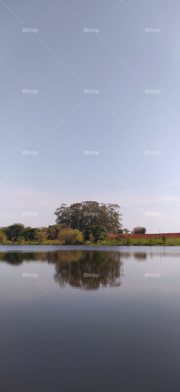 Fim de tarde em lago com reflexo na água no interior de São Paulo.