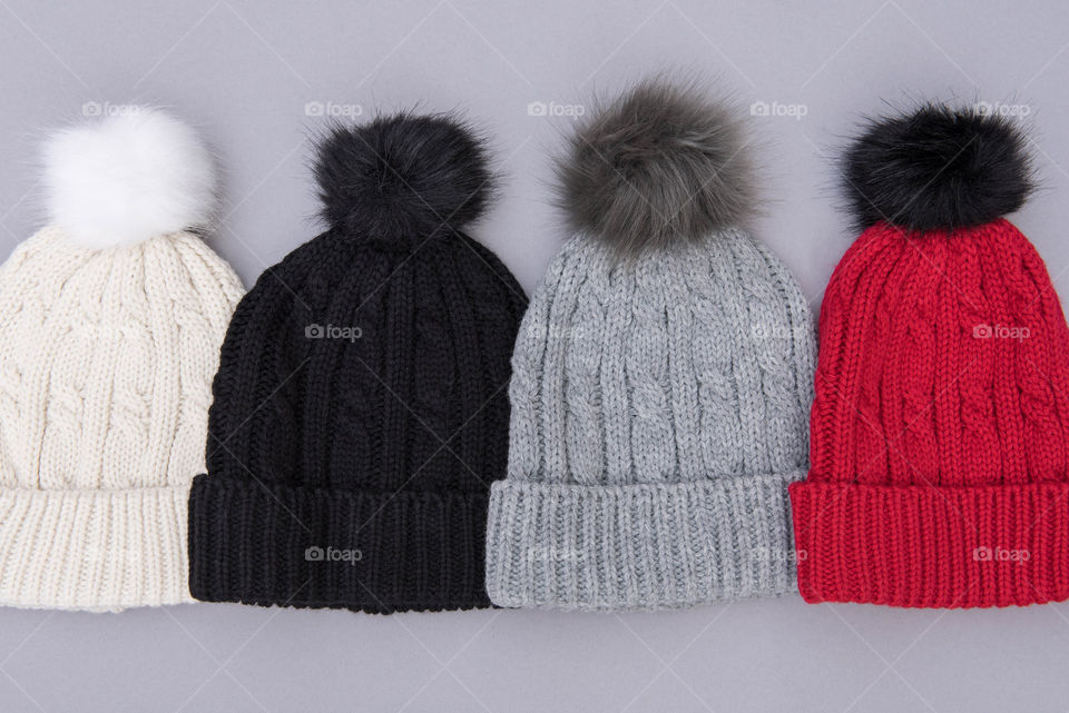 Flat lay of a row of different colored pom pom beanie hats