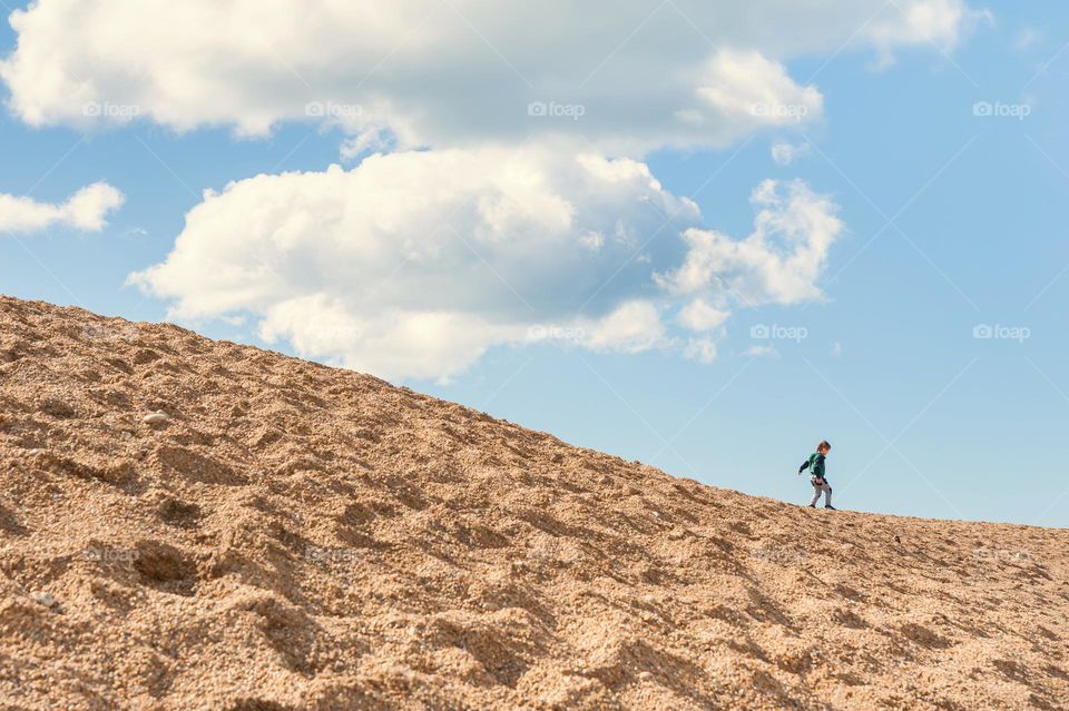 Small boy enjoys running down pebbles dunes against blue cloudy skies.
