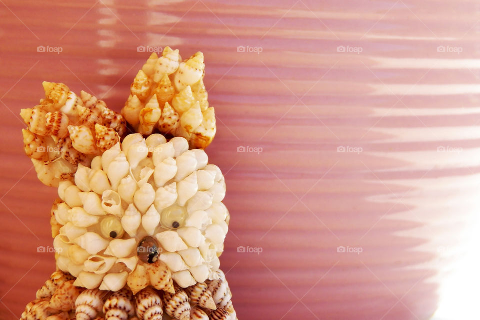 A textured seashells owl representation against à pink lined ceramic container