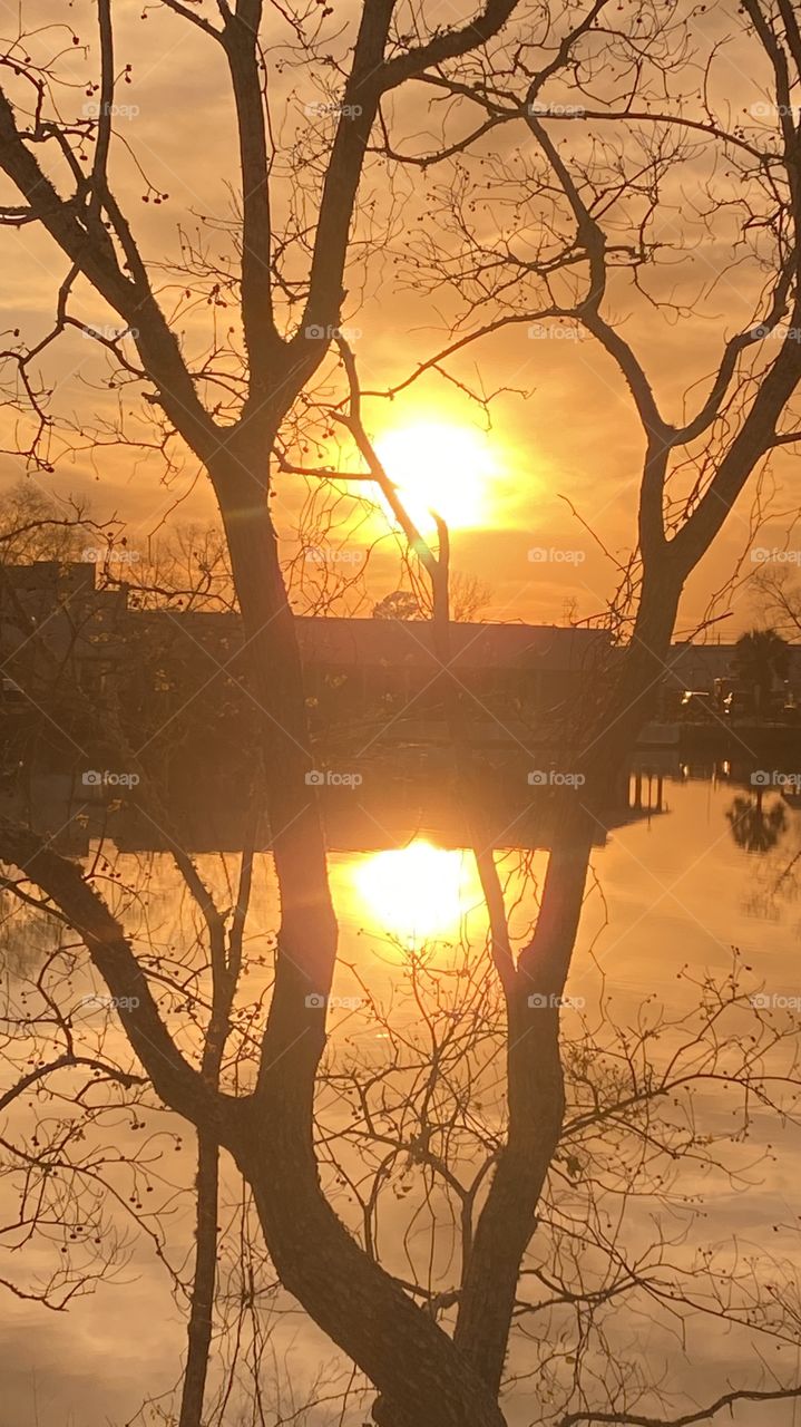 Heading Into Evening High Clouds Partly Separated parting letting in blue sky. Sun glowing with Reflections in water of Lake. Thin Yellow circle around Sun glowing while feathered clouds of Sun.
