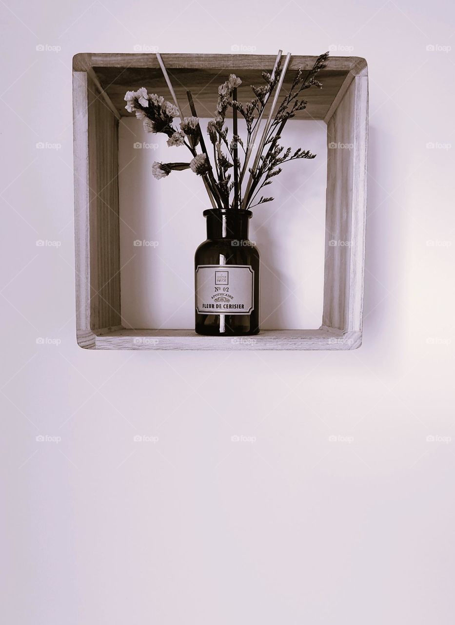 Sepia shot of a vintage looking apothecary bottle filled with dried flowers and placed on a square shelf