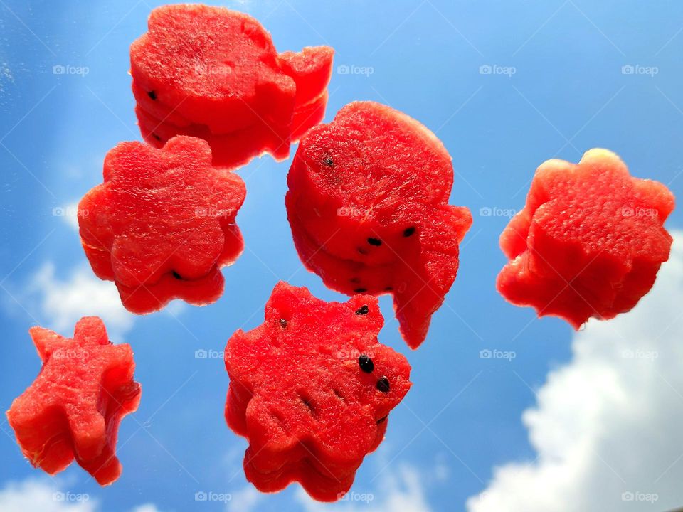 Summer meal. Pieces of red ripe watermelon of various shapes lie on a mirror surface. A blue sky with white clouds reflects on a mirror surface