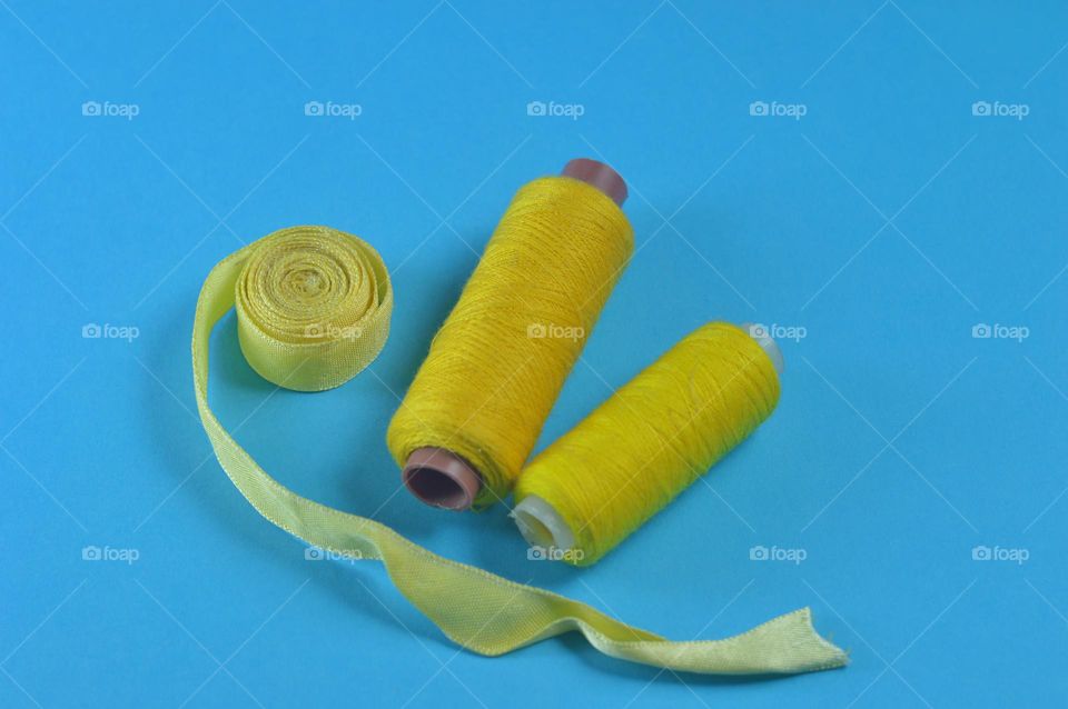 two spools of yellow thread and a yellow skein of ribbon on a blue background