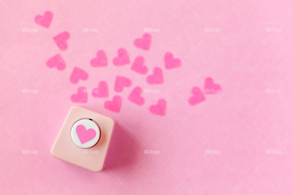 Hole puncher with paper shapes of hearts. Valentine's concept in pink.