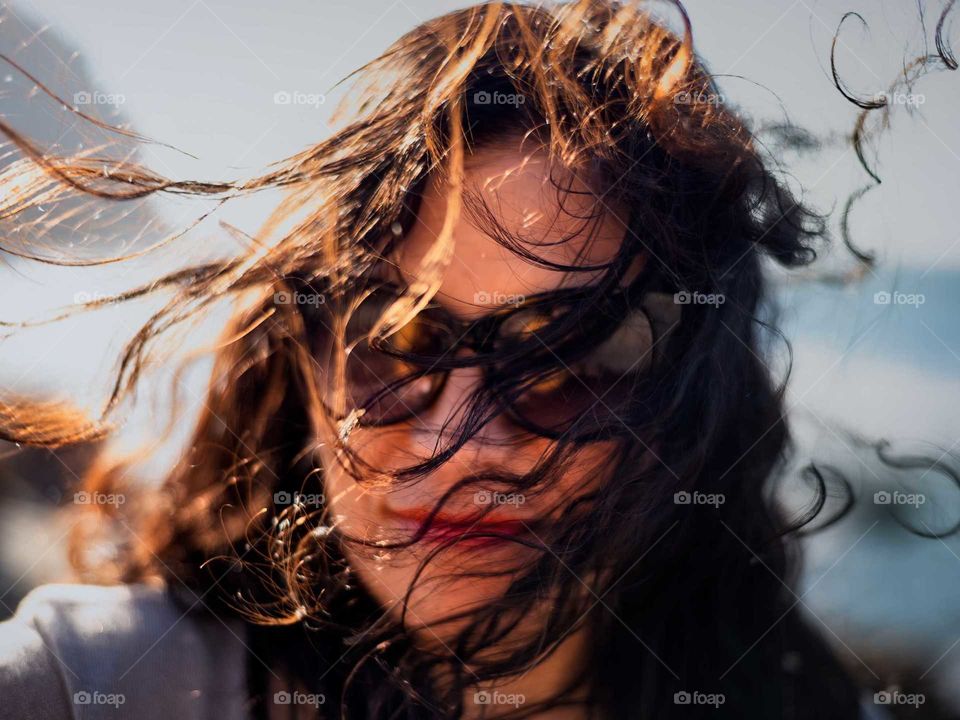 young woman messy hair by the wind dark glasses, face covered by her hair