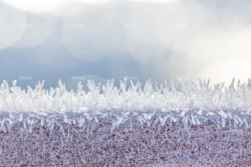 Closeup of frost covering wooden fence on a cold sunny winter day, frozen lake and bokeh in the background