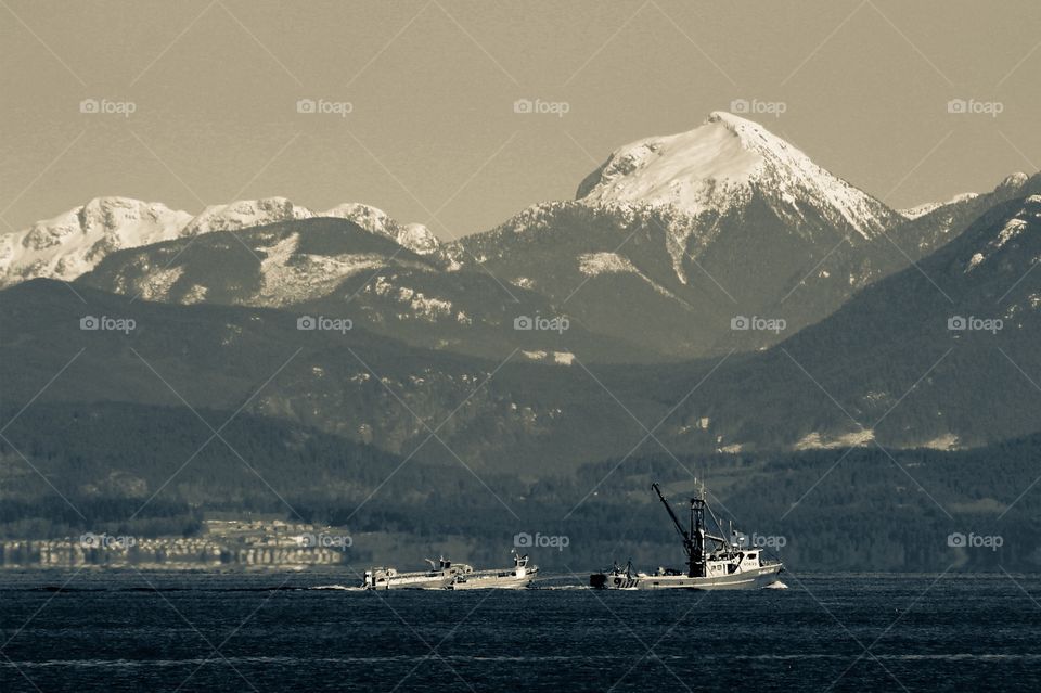 A monochrome landscape of a herring fishing boat pulling 2 smaller boats along the strait. Desktop features were utilized to apply split toning to vary the shades of blue-grey & grey for additional contrast between sea, shore, hills, mountains & sky.