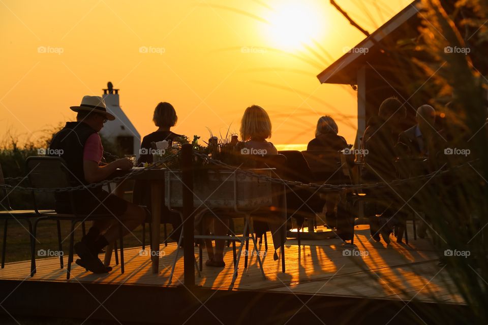 People sitting at a outdoors restaurant in the sunset 