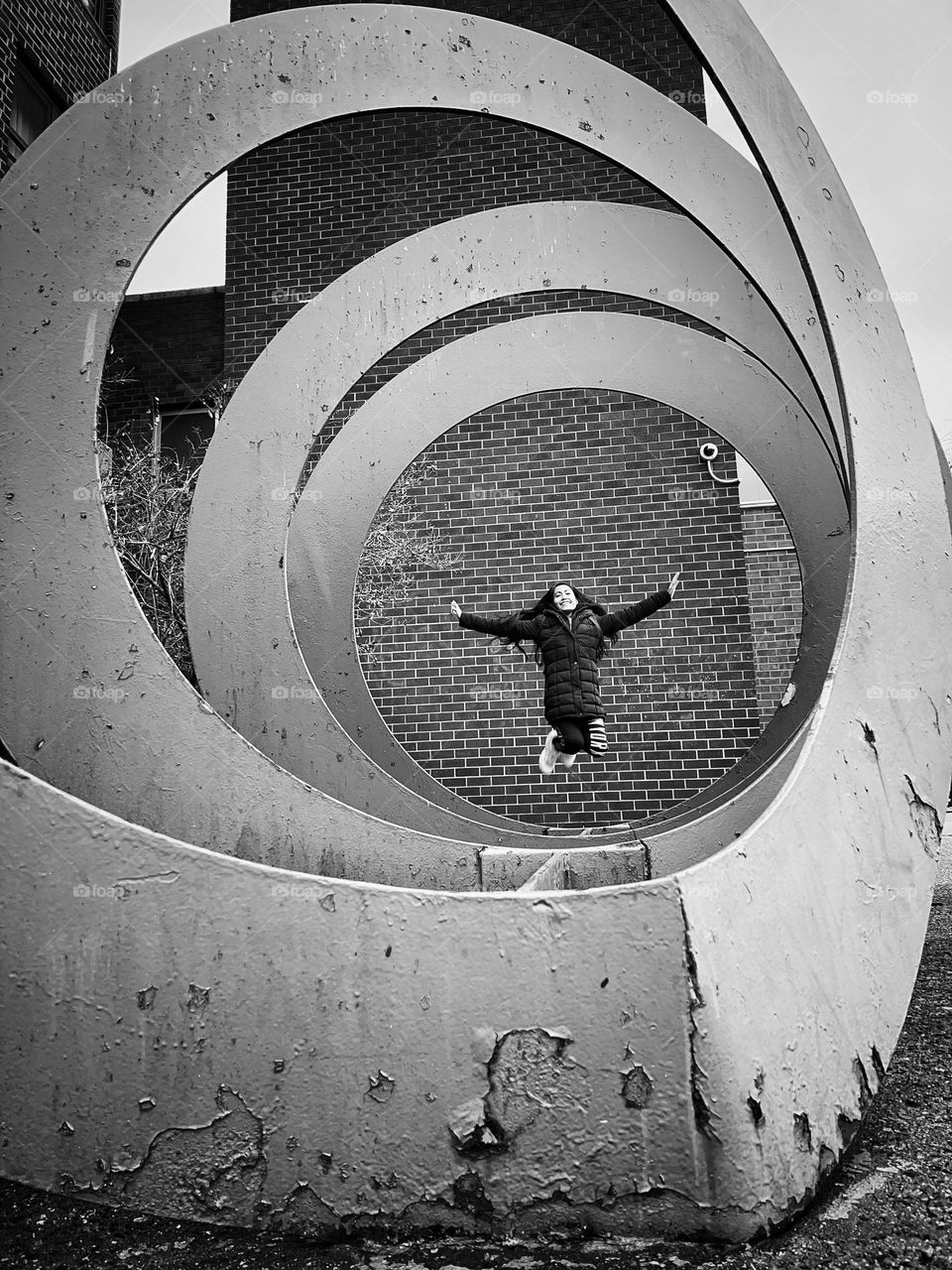 A woman jump with smile on her face against the brick wall and with a circular designed as a framed. 