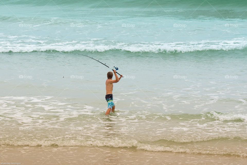 a young man is standing at the waters edge casting a line fishing in the blue ocean water