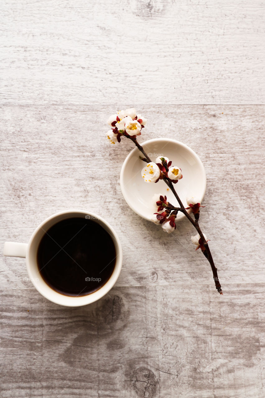Top view of cup with coffee and flowered branch on the wooden table.