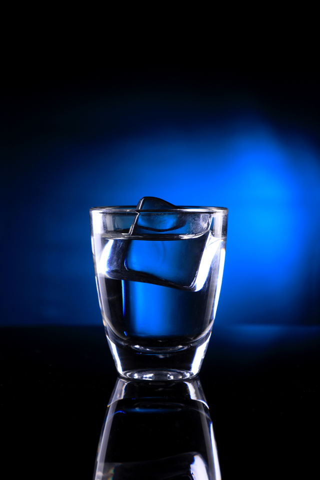 Shot glass on blue background with an ice cube