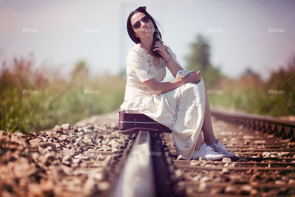 Woman sitting on suitcase over the railroad