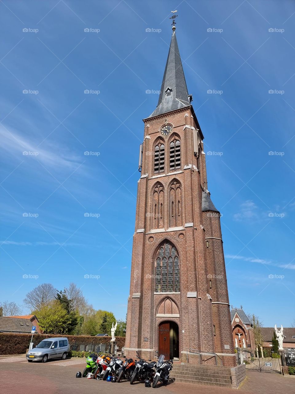 Motorbikes parked in front of the bell tower of a Gothic catholic church on a sunny day