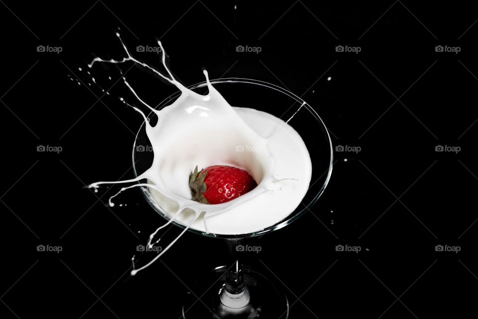 Fresh strawberry falling into glass of milk