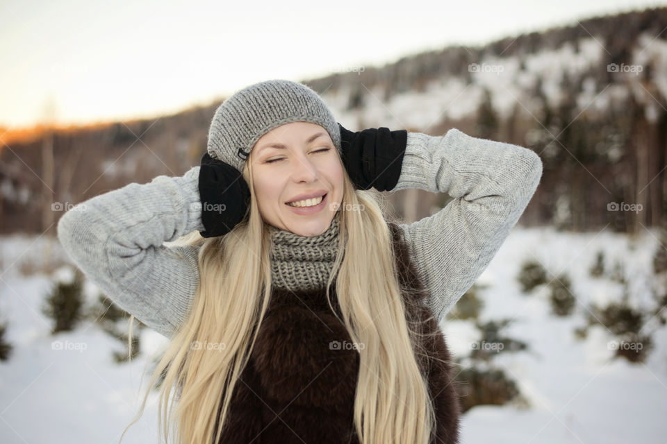 Blonde woman wearing winter hat with hands on ears