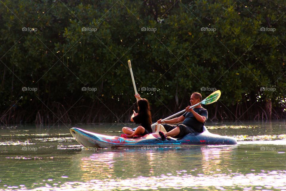 View of a man and a little girl sitting on a canoe pedaling the paddles they are holding during the day, canoe sports playing in the water : Jakarta, Indonesia 11 May 2023