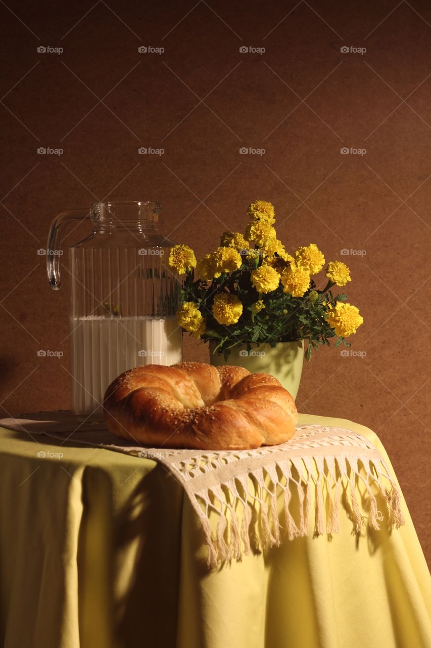 Still life in the studio of a glass jug with milk, rolls of bread, and yellow marigolds on a towel made by my mother