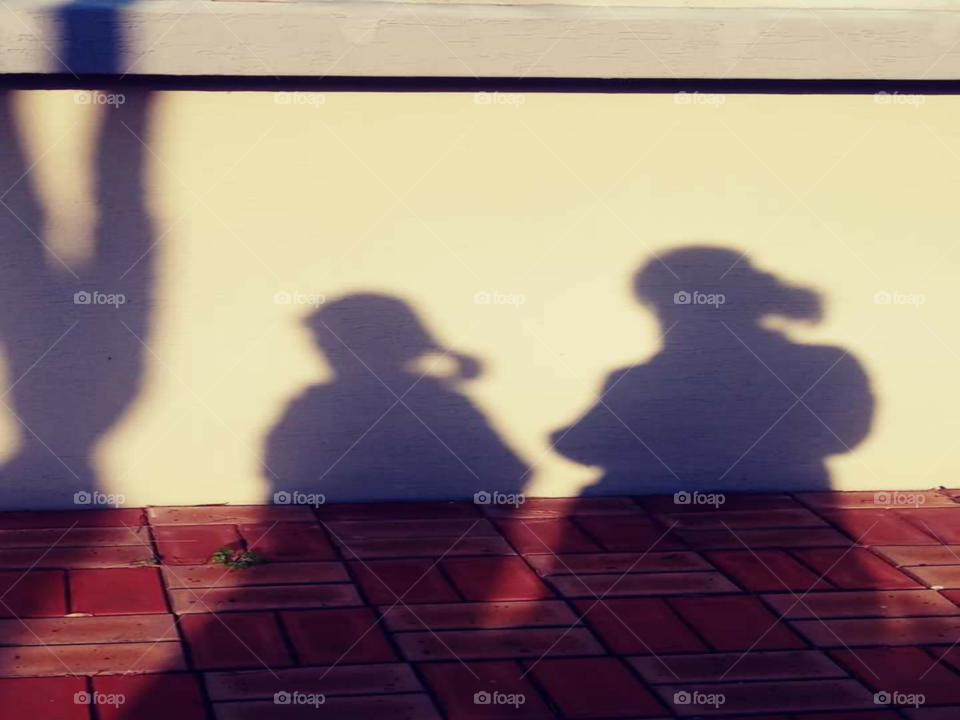 the shadow of a child  and mother. the child is walking away while mother is following  at her back.