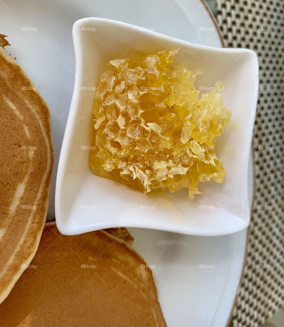 Piece of honeycomb next to pancakes inside white ceramic container, healthy food, healthy breakfast, alternatives to sugar, natural sweetener 