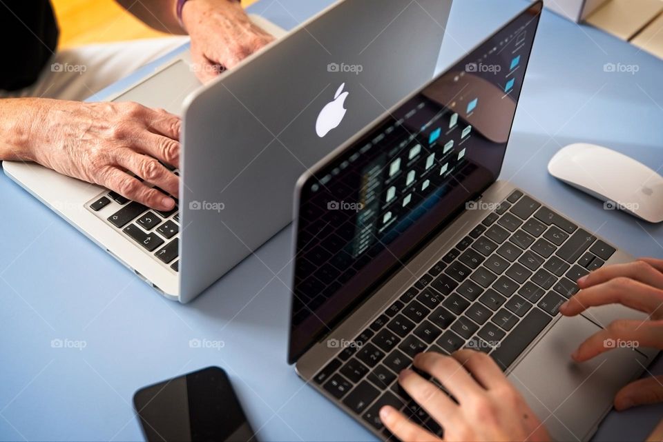 Two people type on Apple laptops 