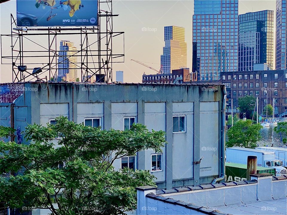 Standing on the staircase of the „Pulaski Bridge“ I am looking out over the parking lot and adjacent buildings in „Long Island City“, Queens. The sun is just about to set. 2023. Hypnotic Productions