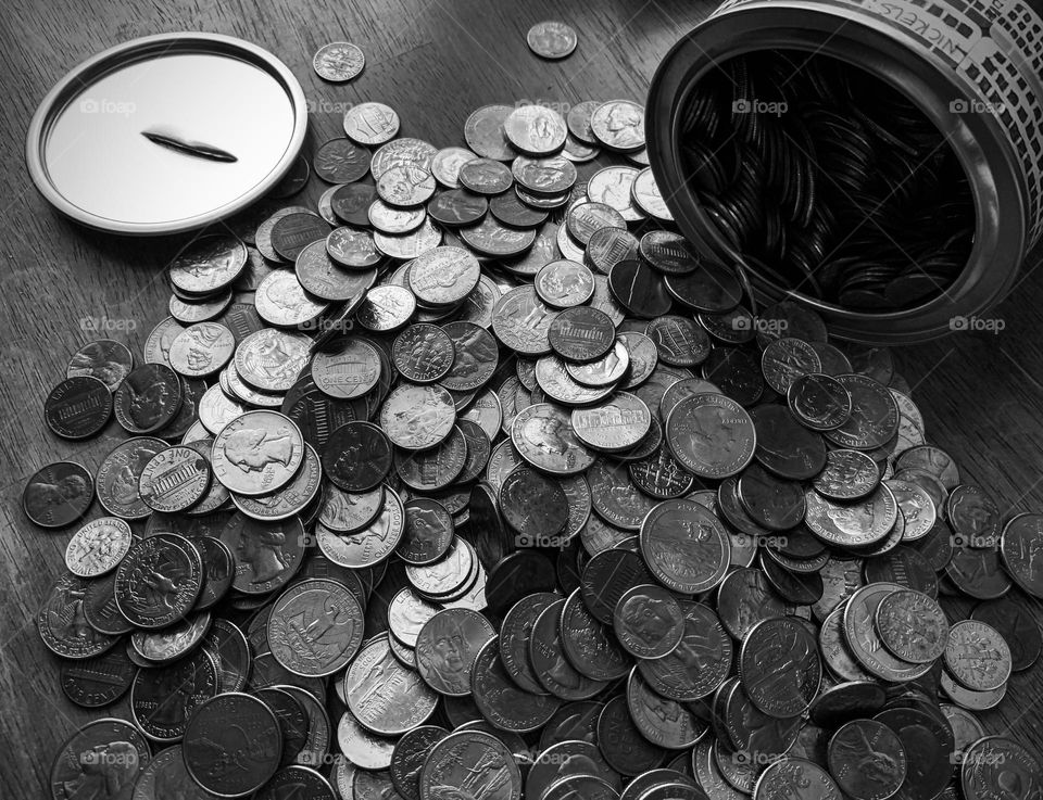 Opening the can full of US coins currency scattered on the table. Black and white.