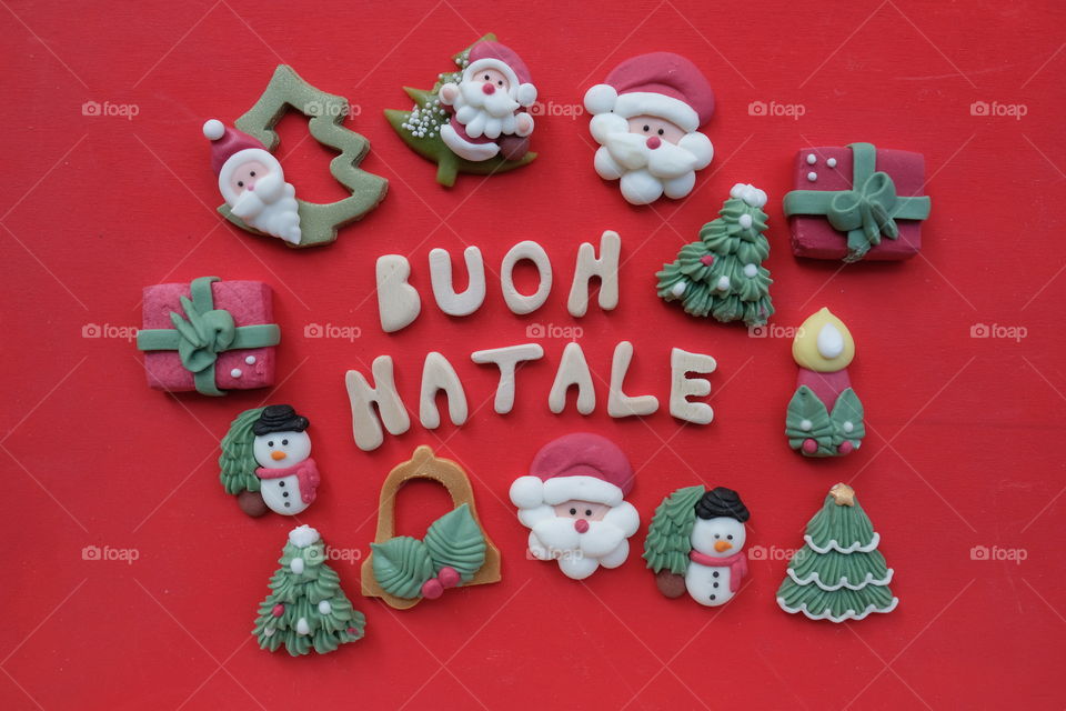 Creative italian Buon Natale, Merry Christmas, composed with handmade wooden letters and marzipan Christmas symbols over red colored wooden board