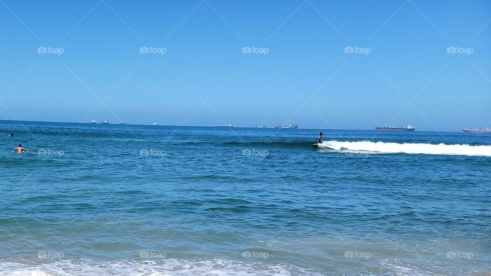 Off in the distance, the cargo ships are lining up, while people swim closer to shore.