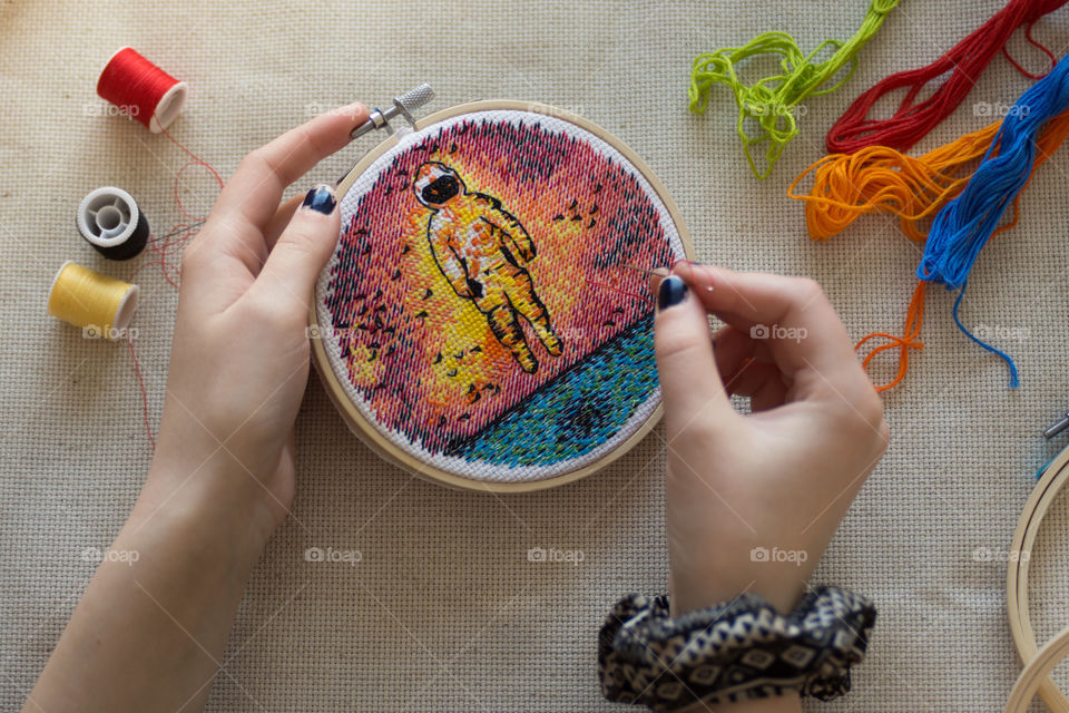 A young woman is an artist that loves cross stitching colorful unique designs with thread in wooden hoops with her hands as her favorite hobby putting a new spin on a traditional art form 