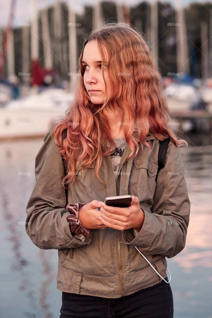 Young woman using mobile phone smartphone standing on a pier over a lake. Candid people, real moments, authentic situations