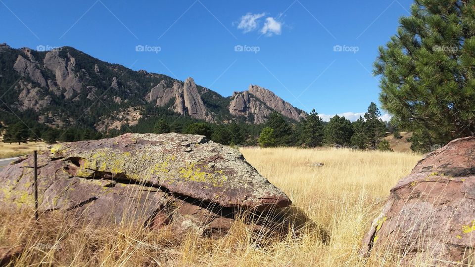 low boulders lies in a golden field before rocky mountainsides