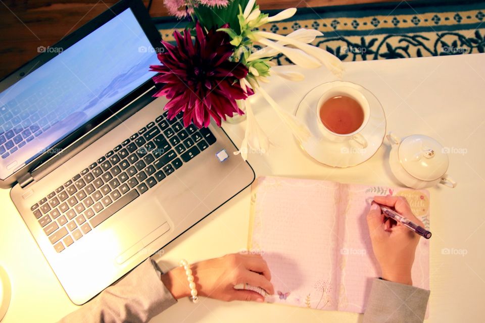 Female writing at desk with laptop flat lay