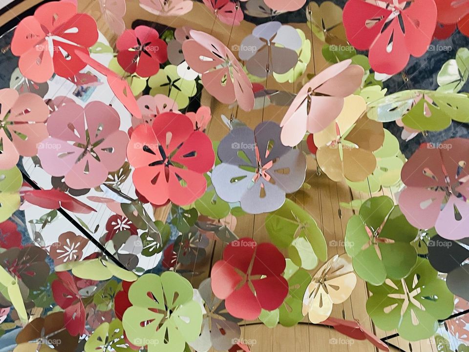 Colorful blossoms in pink, red, green, yellow, and blue hang decoratively from the ceiling, creating a vibrant, whimsical canopy overhead.