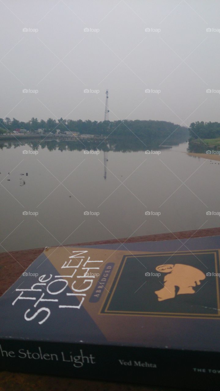 A view of a lake on a cloudy day with a book called The Stolen Light depicted in the photo.