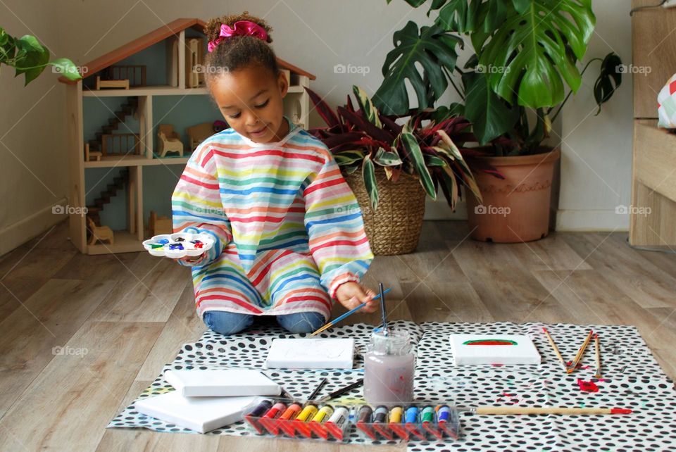 Cute little girl of mixed race painting in an apartment living room - family diversity