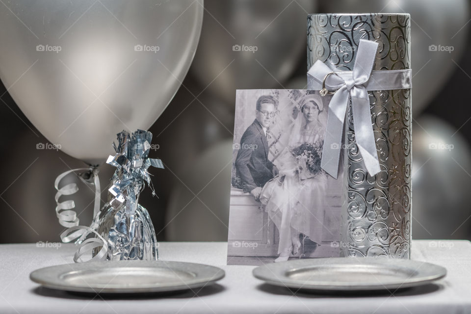 all gray image of anniversary party decorations with a silver gift box, pewter plates, and a black and white vintage photo of a wedding couple in the foreground and silver balloons scattered in the background