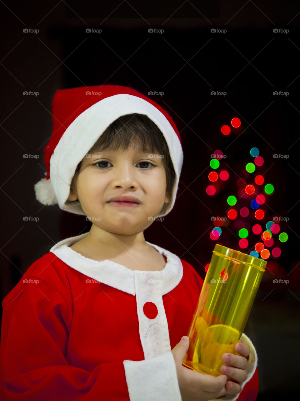 Portrait of a cute little boy Eurasian wearing santaclaus outfit for Christmas party theme celebration at night on a fairy lights bokeh background