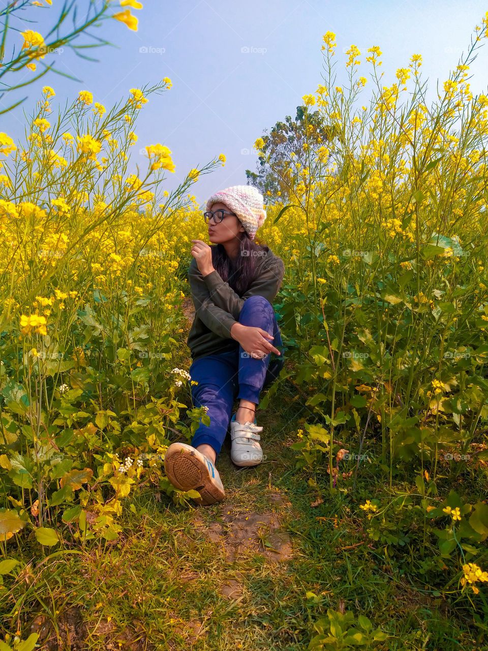 A girl sitting down on a farm of yellow mustards and enjoying mother nature.