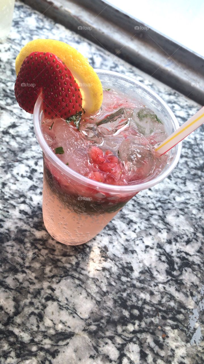 mojito for the hot summer time , cold refreshing drink made with strawberry , lemon, ice , small pices of mint ,soda , and a piece of of both the strawberry and the lemon 