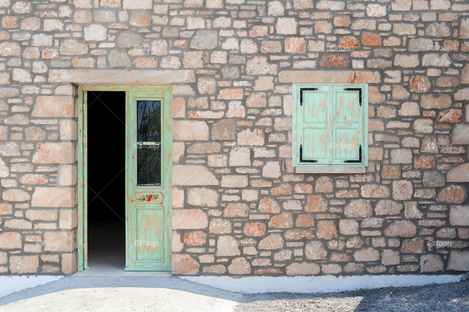 Facade of an old masonry house with green half opened door and closed square window.