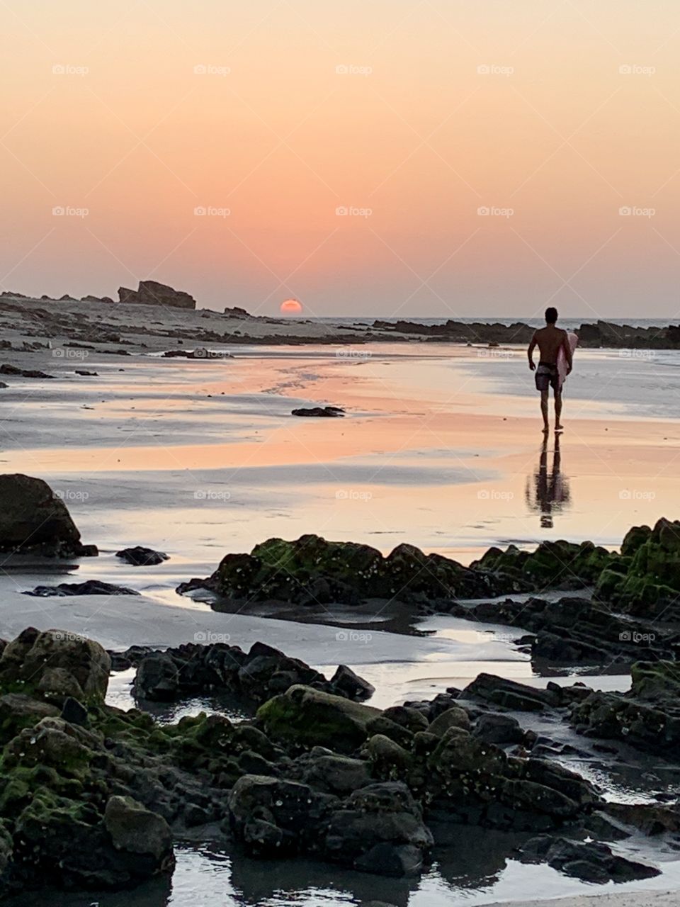 Boy with surf walking in the beach at sunset 
