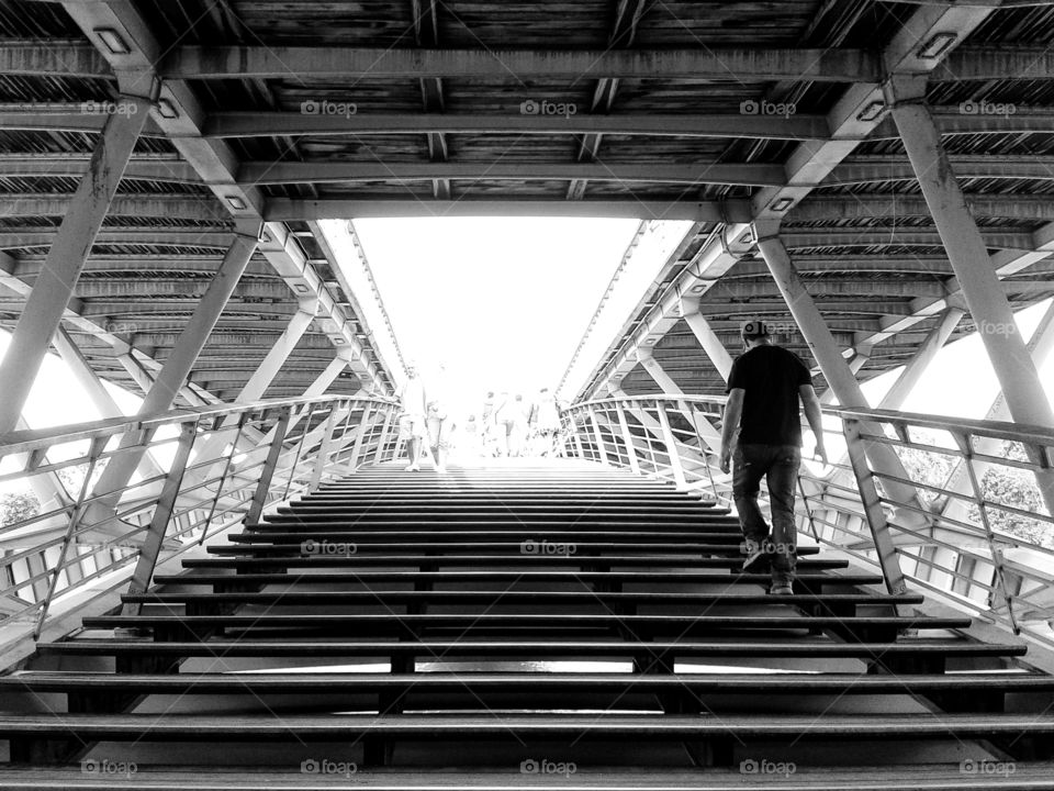 on the way up. a guy walking upstairs on a pedestrian metallic bridge over the Seine river in Paris.