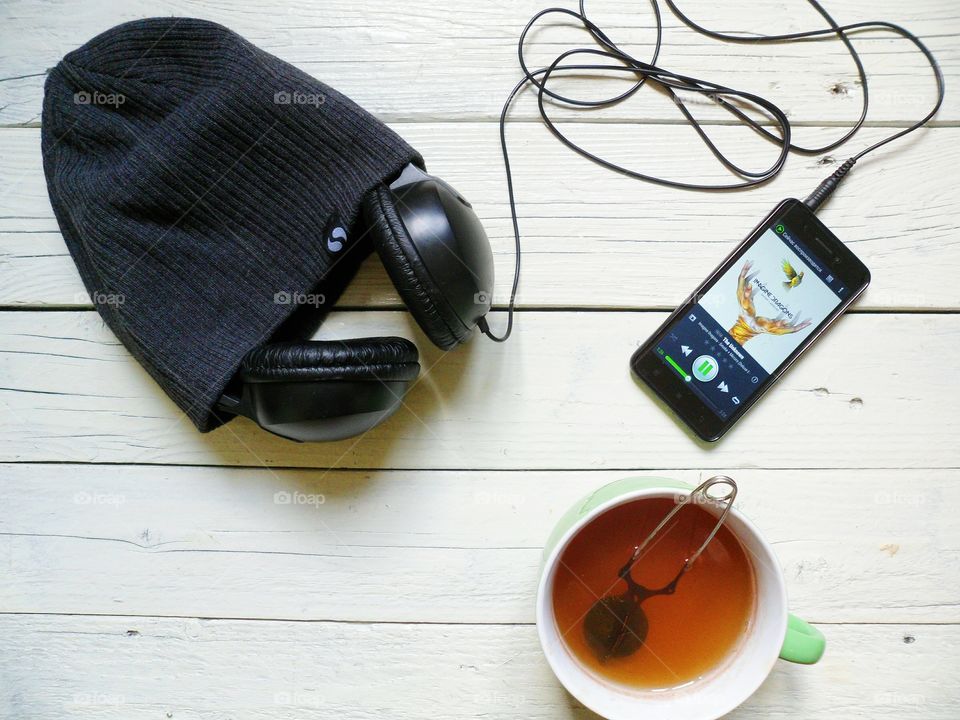 A cup of tea, a smartphone, headphones and a hat